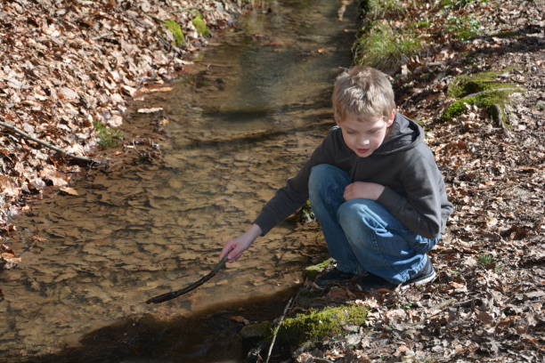 istock Boy in a brook plays with  branch in the water 655724898