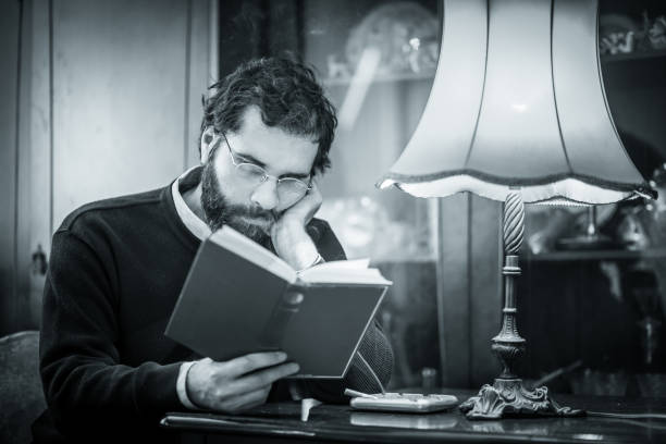 istock Handsome, middle age, bearded man reading book in his home under the lamp light. He is focused. Shallow DOF, focus on face. Some grain added 655752058