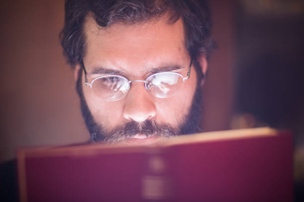 istock Handsome, middle age, bearded man reading book in his home under the lamp light. Close up. He is focused. Shallow DOF, focus on eyes 655752076
