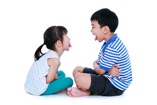 Bad behavior. full body of asian children sticking out tongues and mocking each other. Sister and brother sitting at studio, isolated on white background.