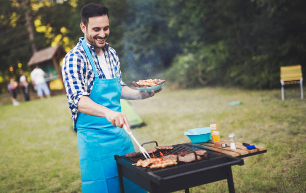 gut aussehend glücklich männlich vorbereitung grill im freien für freunde - barbecue chicken stock-fotos und bilder