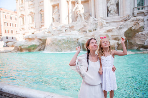 Mom and kid trowing coin at Trevi Fountain for good luck. Little girl making a wish to come back to Rome Young beautiful woman and little girl near fountain Fontana di Trevi triton greek god stock pictures, royalty-free photos & images