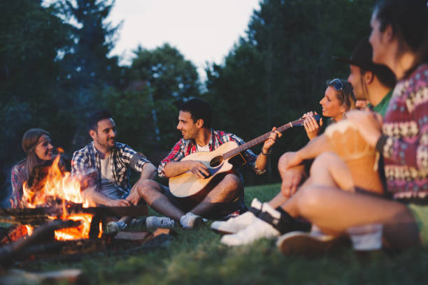 happy friends playing music and enjoying bonfire in nature - friendly fire imagens e fotografias de stock