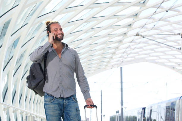 istock Smiling man with cell phone walking with suitcase 655811340