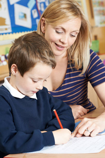 istock Teacher Helping Male Elementary Pupil Working At Desk 655813670