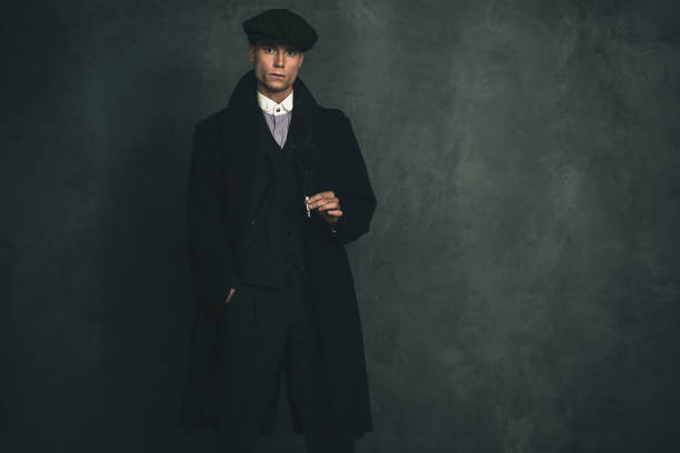 istock Macho retro 1920s english gangster wearing black coat and flat cap holding cigarette. 655820708