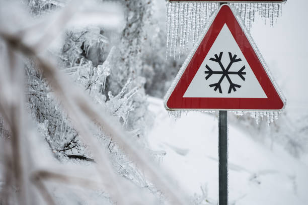 Traffic sign for icy road with sleet covered trees. Danger on the road, black ice danger, wintertime concept.