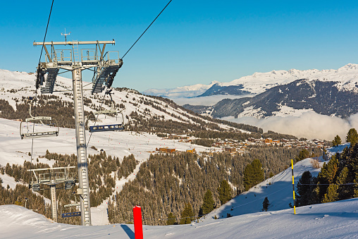 Panoramic view down snow covered valley in alpine mountain range with conifer pine trees and ski lift