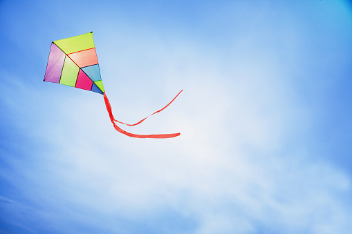 angle view of a colorful kite flying with waving red bow in a deep blue sky with the light of the sun