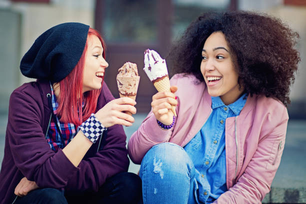istock Two girlfriends are sitting on the stairs and making cheers with ice creams 655954274
