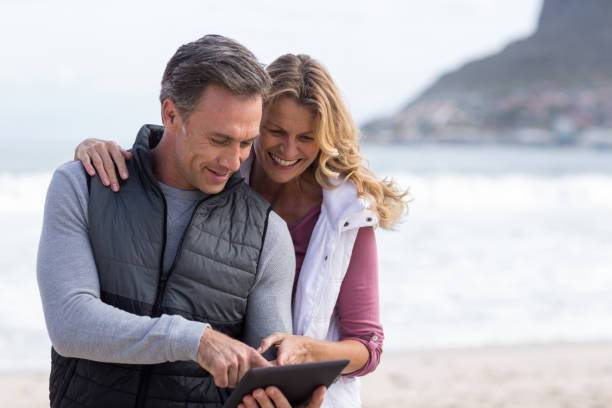 pareja con tabla digital en la playa - standing digital tablet couple love fotografías e imágenes de stock