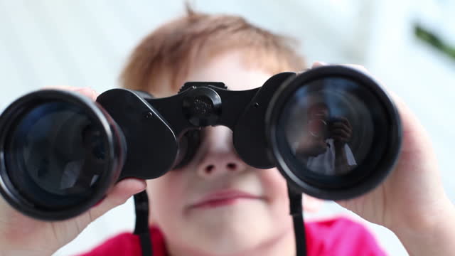 A young boy smiles, then looks through binoculars.