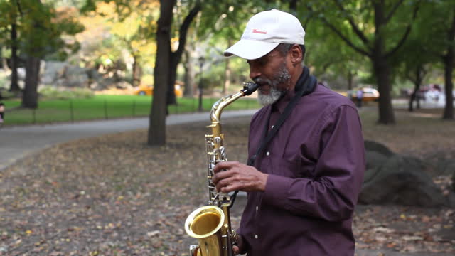 A street musician plays a saxophone in a park.