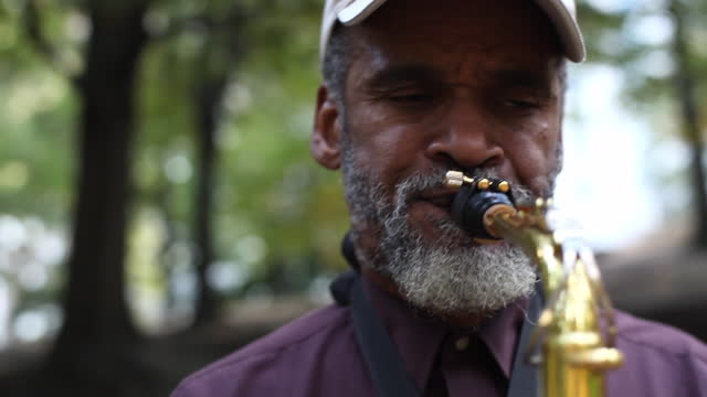A street musician plays a saxophone in a park.