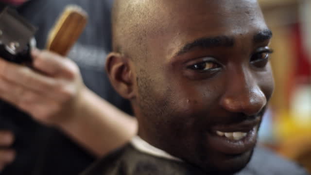 A barbershop customer smiles while getting his head shaved.