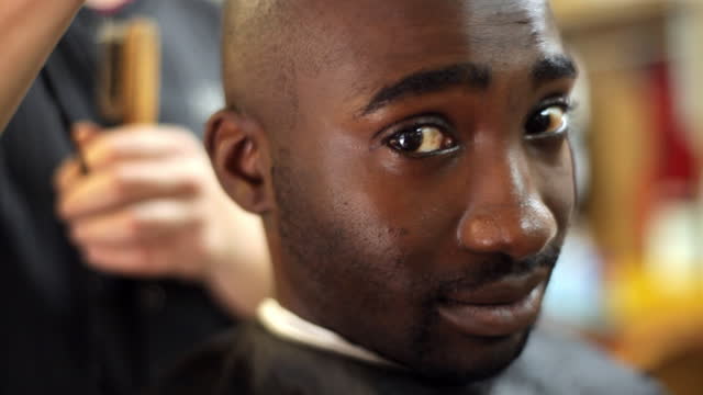 A barbershop customer smiles while getting his head shaved.