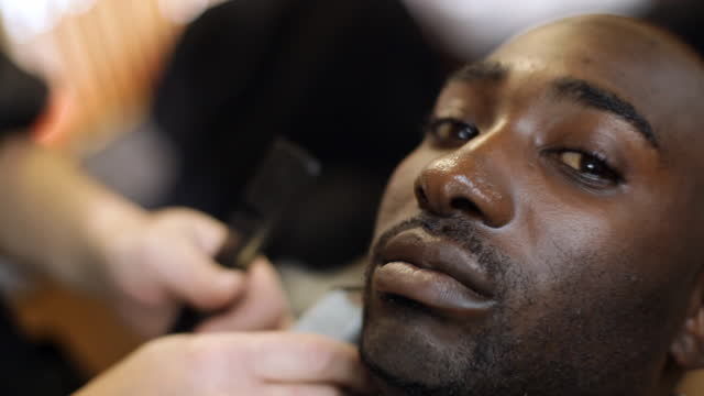 A barber shaves a customer's goatee.