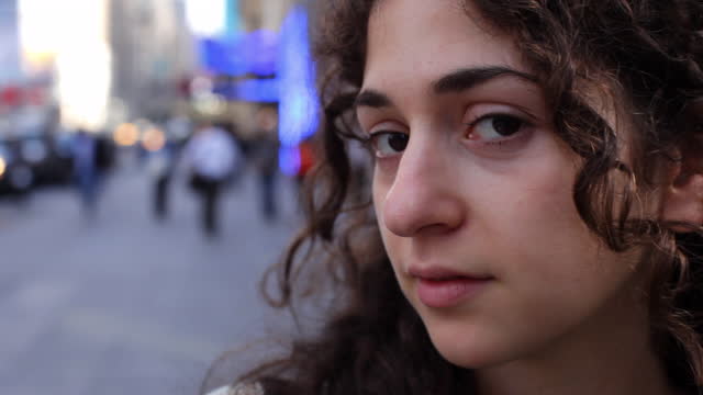 Tilt up from sweater to profile young woman's face on NYC sidewalk   turns eyes to look at camera