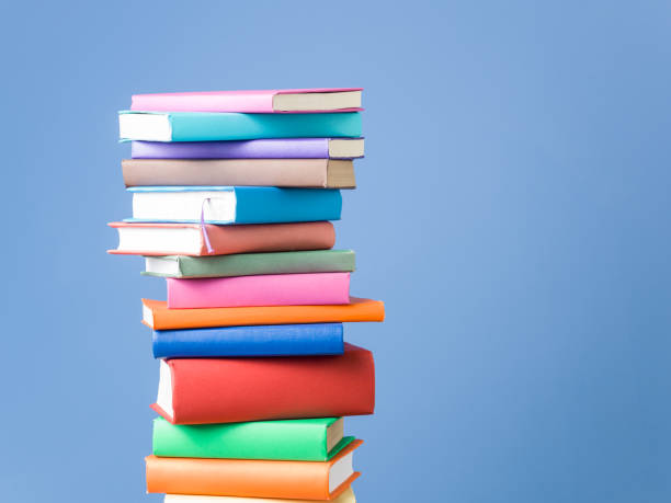 stack of multi colored books on blue background - stacking imagens e fotografias de stock