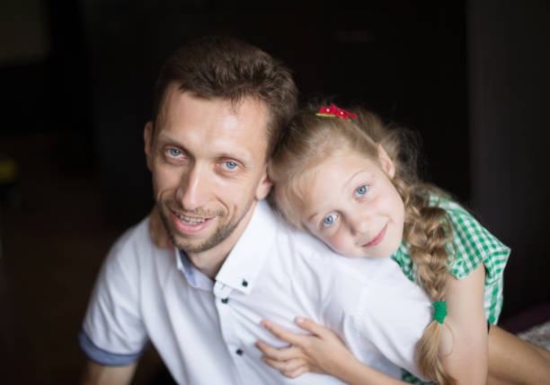 toddler son sitting on father's shoulder on a walk in the backyard with a salmon colored wall in the background.