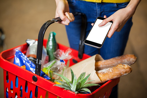 Mid section of woman holding groceries and mobile phone in supermarket