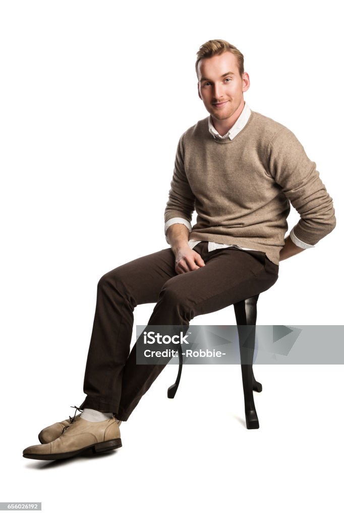 Attractive man smiling wearing sweater Handsome blonde man wearing a brown pullover and white shirt, sitting down smiling against a white background. Sitting Stock Photo