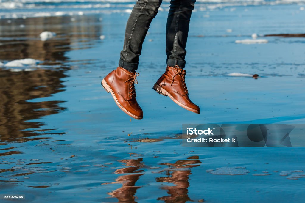 Jumping in Boots Jumping up and down on reflective wet sand in brown leather boots Jumping Stock Photo