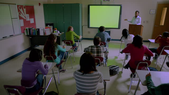 A high school teacher gives a lecture to a diverse class of students.