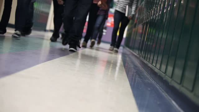 A group of high school students walk down the hall past lockers toward class.