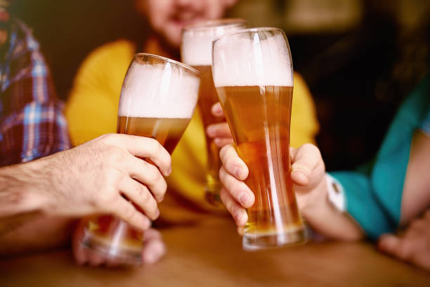 Cheers to St Patrick! Closeup shot of three elegant tall glasses with delicious craft lager beer and high viscous foam in hands of men meeting round table in Irish Pub ale stock pictures, royalty-free photos & images