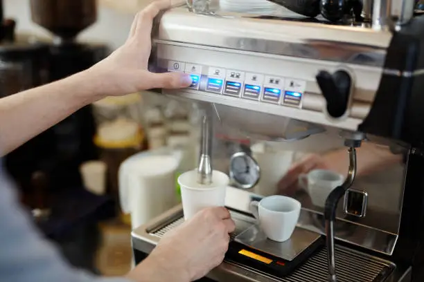 Barista pushing steam button to froth milk for cappuccino