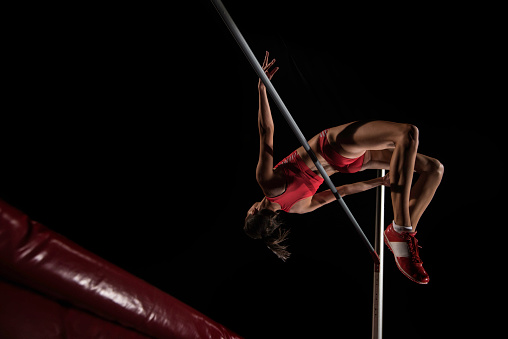 Female athlete in mid air performing a high jump over a horizontal bar.
