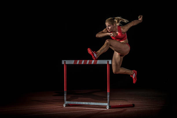 female athlete hurdling at a running track at night - hurdling hurdle running track event imagens e fotografias de stock