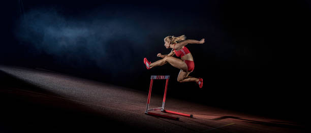 atleta femenina claro un obstáculo en una pista en la noche - hurdling hurdle running track event fotografías e imágenes de stock