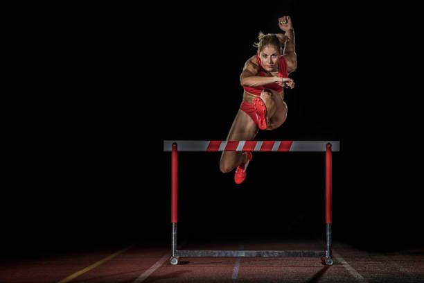 istock Female athlete hurdling at a running track at night 656078564