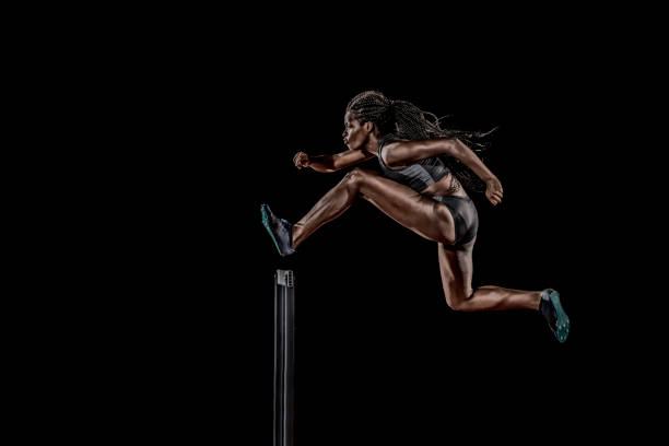 Side view of a woman jumping over a hurdle Side view of a woman of african ethnicity jumping over a hurdle. hurdling track event stock pictures, royalty-free photos & images