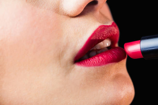 Close-up of beautiful woman applying red lipstick on lips against black background