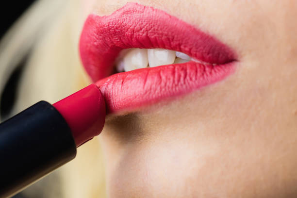 Close-up of beautiful woman applying red lipstick on lips against black background