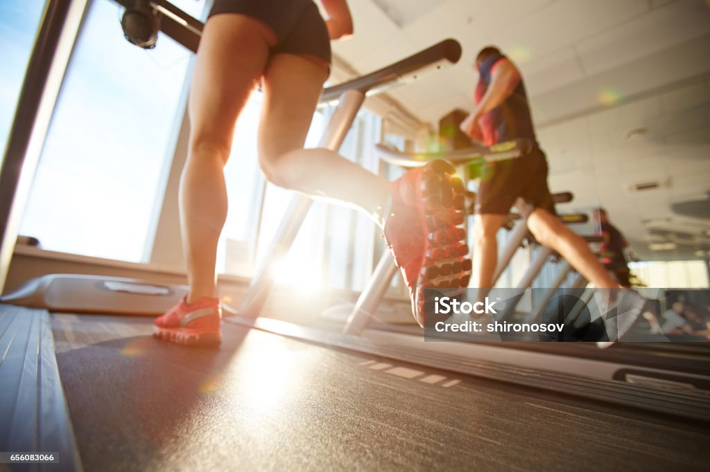 Morning on treadmill Female athlete in mini shorts warming up on treadmill on beautiful sunny morning Gym Stock Photo