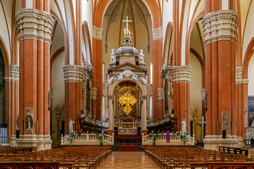 Wide-angle interior view of the Basilica of San Petronio, Piazza Maggiore, Bologna, Italy showing the marble columns and ornate gilded cross above the altar.
