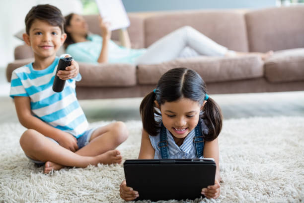 boy watching television and girl using digital tablet in living room - digital tablet women enjoyment happiness imagens e fotografias de stock