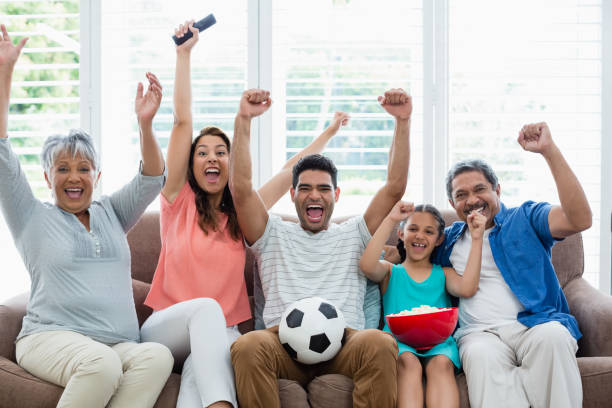 幸せな多世代家族見てサッカーの試合をリビング ルームのテレビで - fan television football watching tv ストックフォトと画像