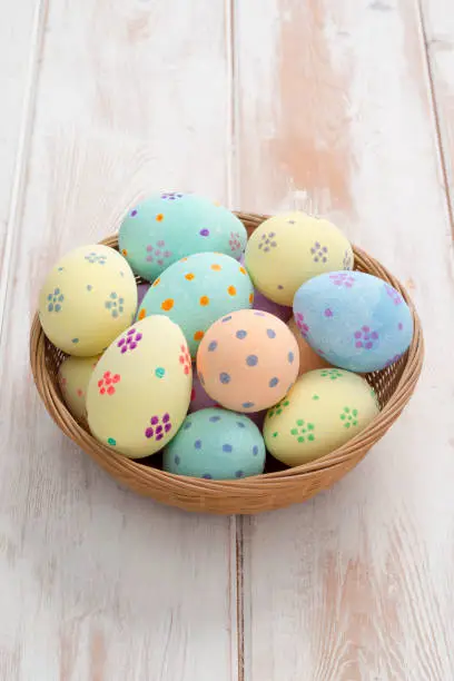 Pastel-colored painted eggs in a wicker bowl over a wooden panel background