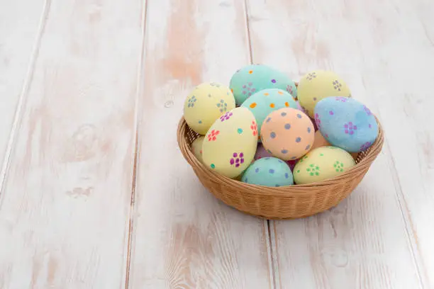 Colorful hand-painted easter eggs in a wicker bowl on a wooden panel background with copy space