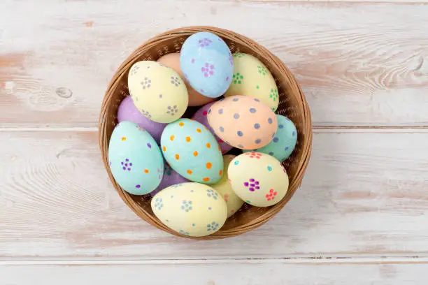 Overhead shot of colorful easter eggs in a wicker bowl over wooden panel background