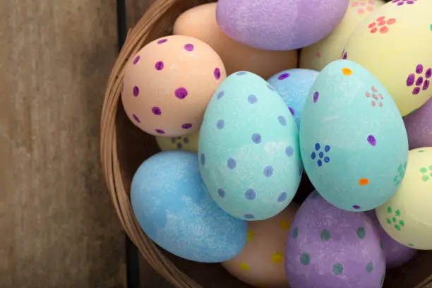 Close up of painted pastel easter eggs in a wicker bowl over a wooden background with copy space