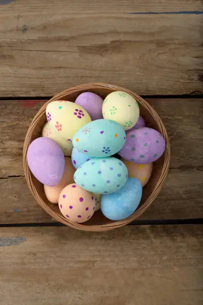 Overhead shot of easter eggs in a wicker bowl over a wooden background