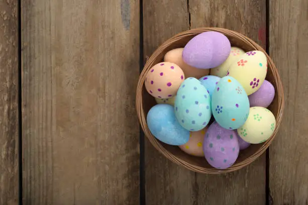 Overhead shot of hand-painted eggs in a wicker bowl over a wooden background with copy space