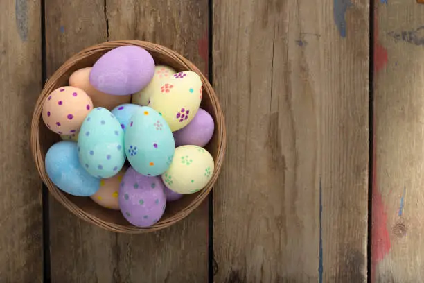 Overhead shot of easter eggs in a wicker bowl over a wooden background with copy space
