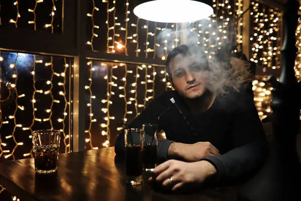 Photo of man holding hookah pipe and smoking in a night club